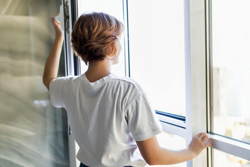 Lüften stärkt Immunabwehr - Junge Frau öffnet Fenster für frische Luft.